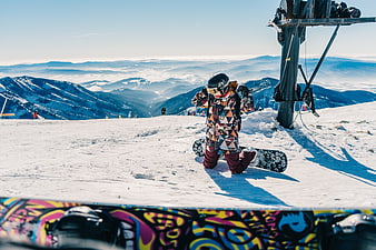 Snowboarder kneeling on snowy mountain peak with ski lift