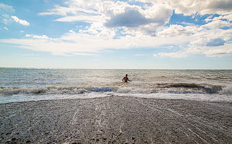 Man Walking in Ocean Waves on Pebble Beach