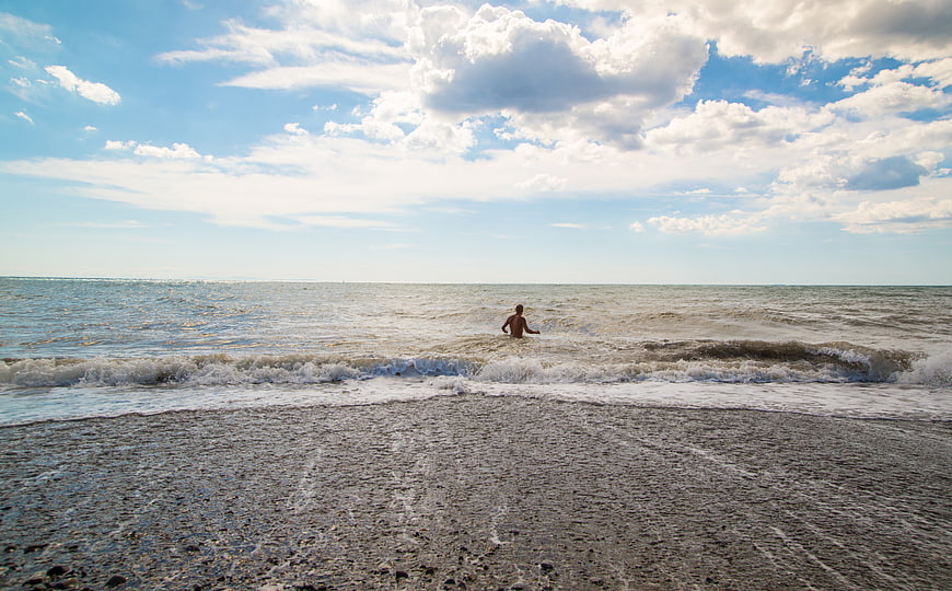 Man Walking in Ocean Waves on Pebble Beach