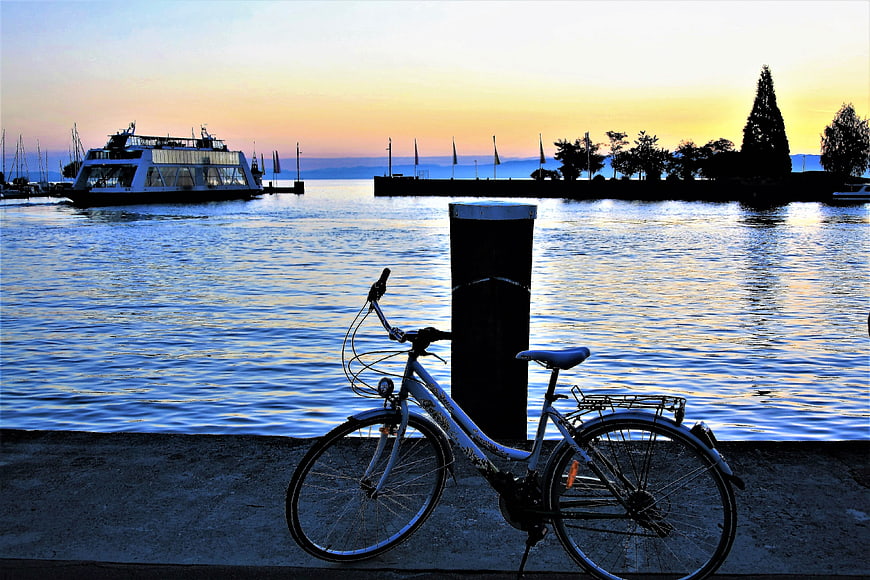 White bicycle parked by lake at sunrise with ferry