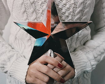 Woman holding shiny star ornament in white sweater