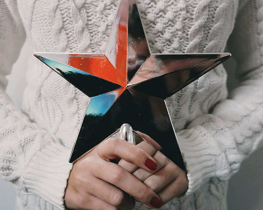 Woman holding shiny star ornament in white sweater