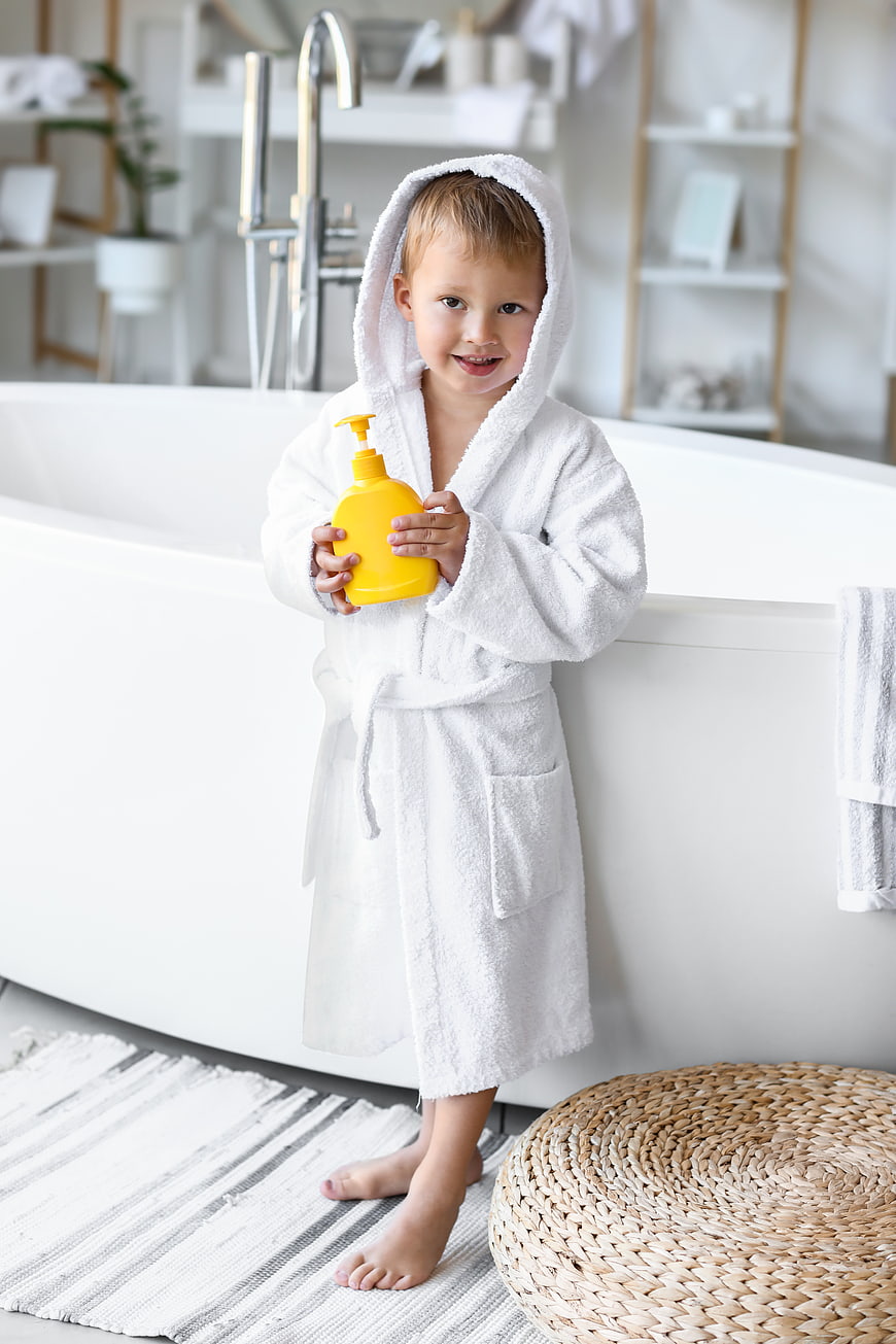 Cute child in white bathrobe holding yellow soap bottle