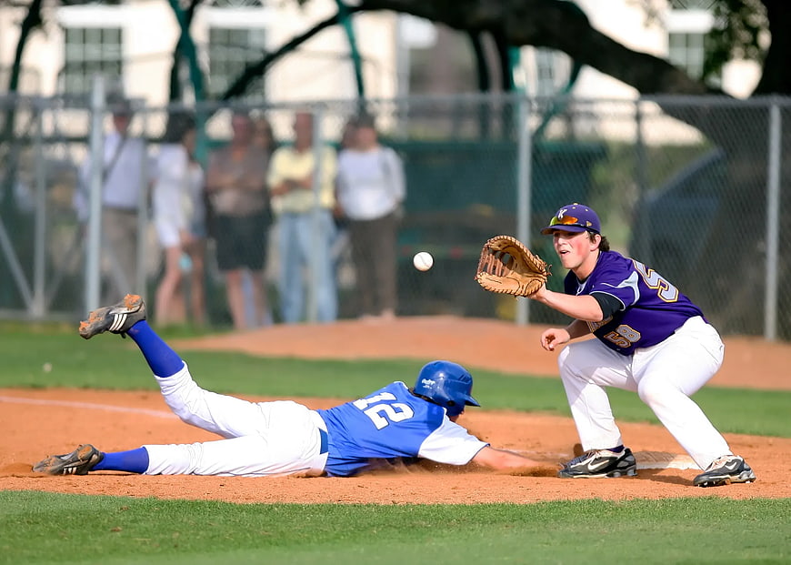 Baseball player sliding into base while fielder catches ball