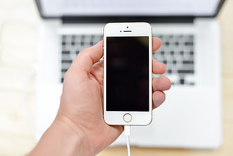 Hand holding white smartphone with laptop background