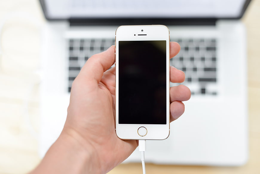 Hand holding white smartphone with laptop background