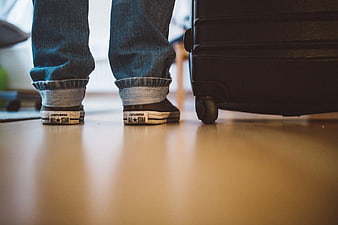 Low angle view of feet in sneakers next to suitcase