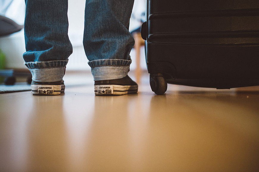 Low angle view of feet in sneakers next to suitcase