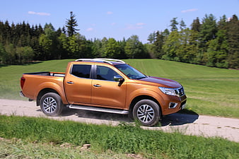 Orange Nissan Navara Pickup Truck Driving On Gravel Road In Countryside