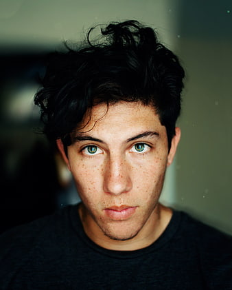 Close-up portrait of a young man with dark hair and green eyes