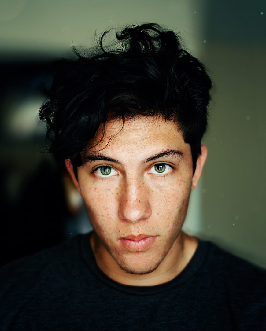Close-up portrait of a young man with dark hair and green eyes