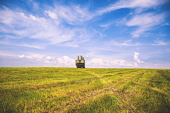 Truck with Hay Bales in Green Field Under Blue Sky