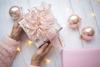 Hands holding pink gift box with ribbon and Christmas ornaments