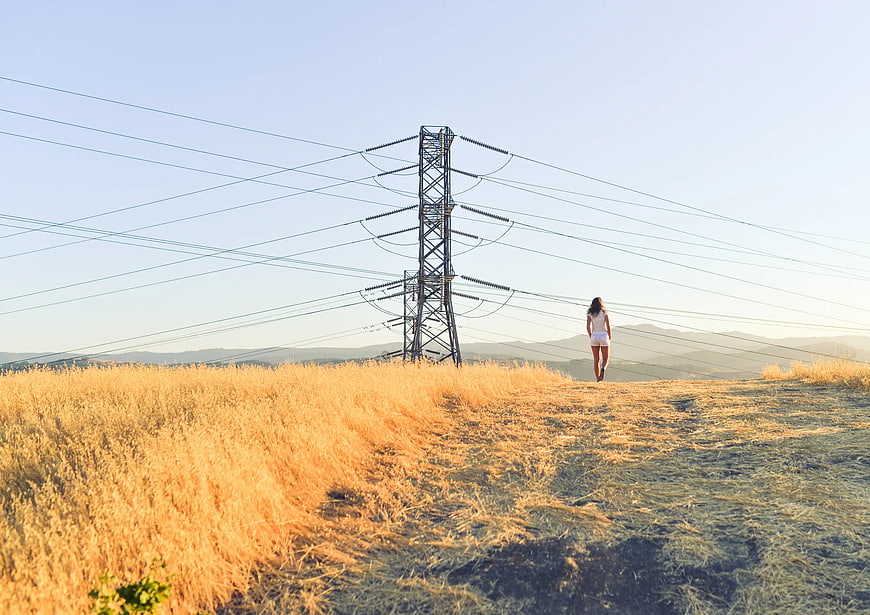 Woman Walking Near High Voltage Tower in Golden Field