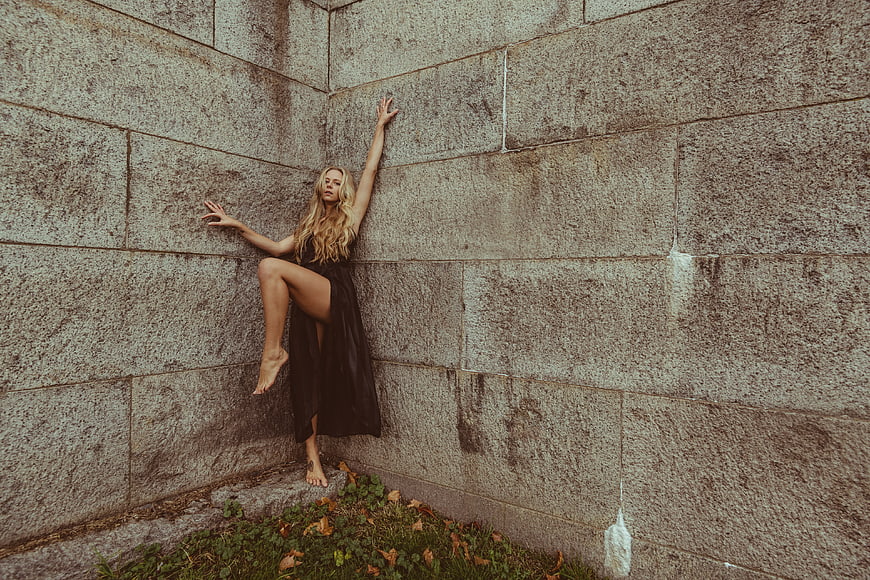 Blonde woman in black dress posing against stone wall