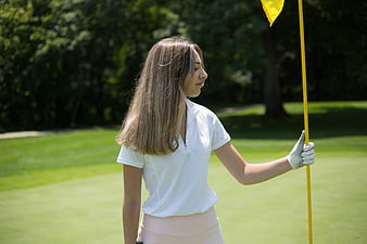 Young female golfer holding yellow flag on green