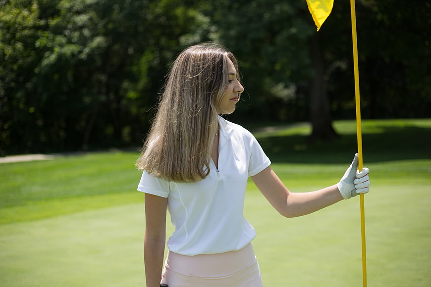 Young female golfer holding yellow flag on green