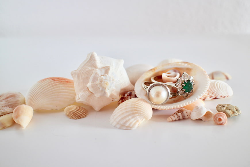 Vintage pearl and emerald rings displayed on seashells