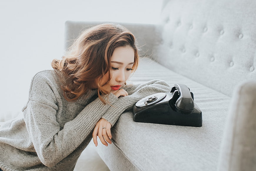 Sad Asian Woman Waiting by Vintage Rotary Phone on Sofa