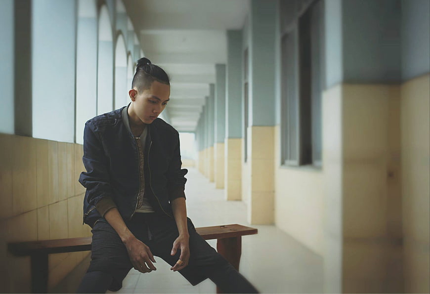 Pensive Asian Man Sitting Alone on Bench in Hallway