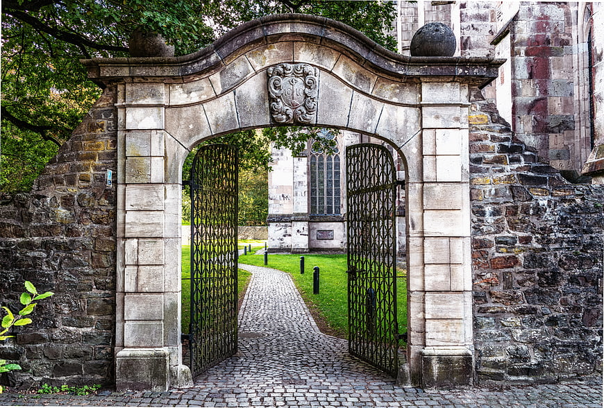 Historic stone archway gate with open iron doors leading to church