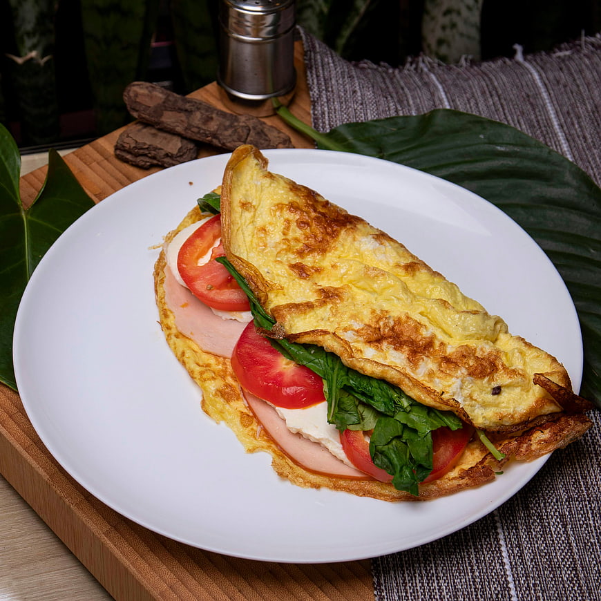 Homemade omelet with ham, cheese, spinach, and tomatoes on white plate