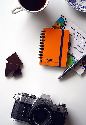 Flat lay of vintage Canon camera, orange notebook, and coffee