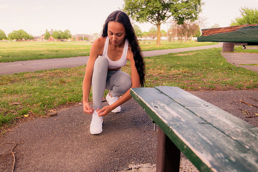 Woman tying shoelaces on park bench before workout