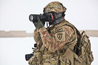 Soldier in camouflage taking photo with DSLR camera in snow