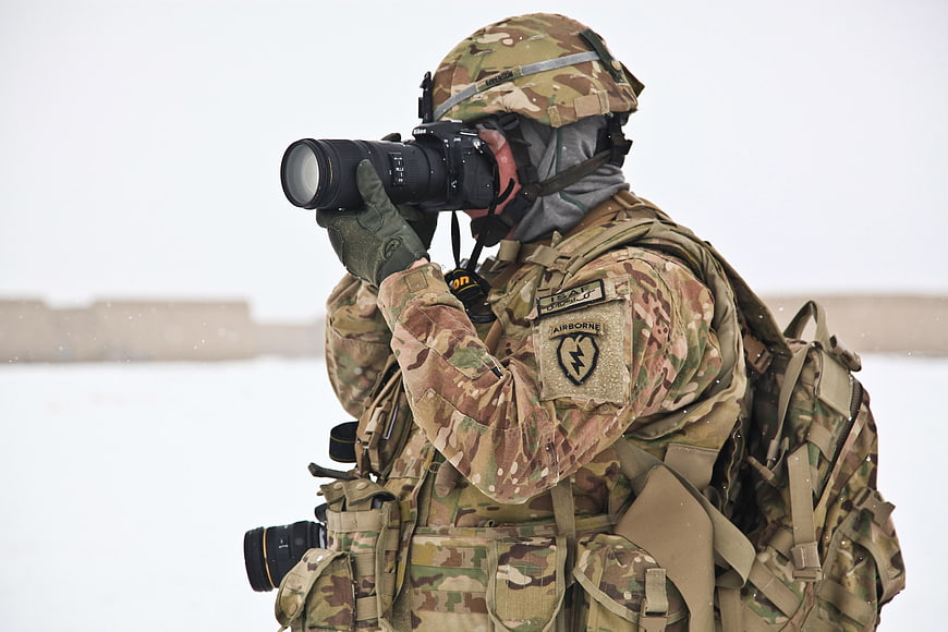 Soldier in camouflage taking photo with DSLR camera in snow