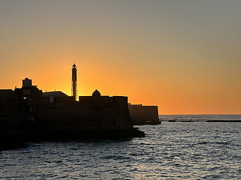 Silhouette of Lighthouse and Fort at Sunset Over Ocean
