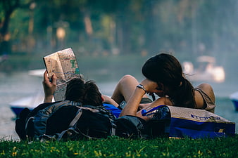 Young couple relaxing on grass reading map near lake
