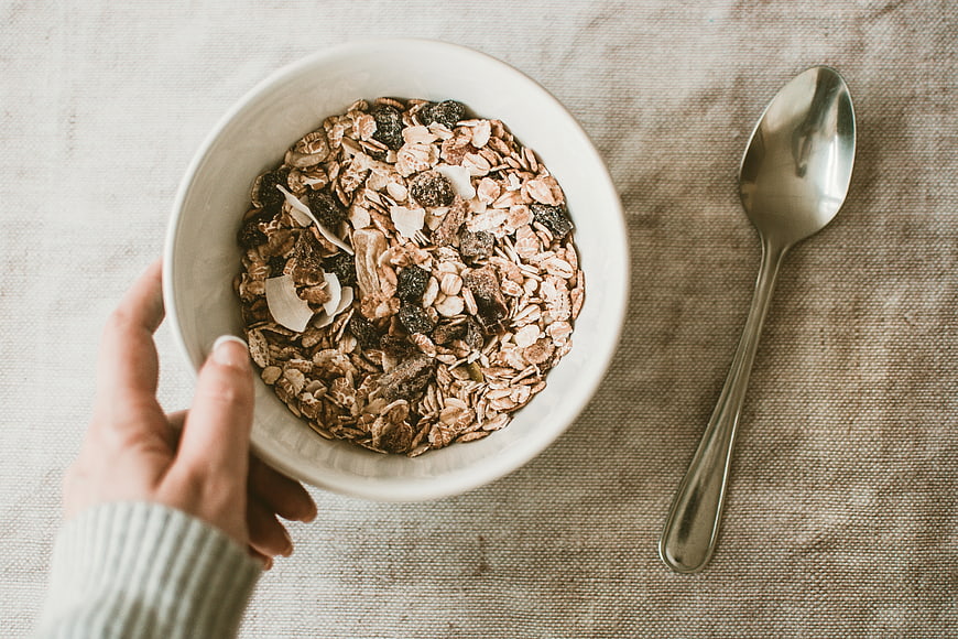 Top View of Hand Holding Bowl of Granola and Spoon