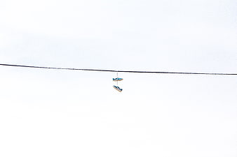 Minimalist sneakers hanging on a wire against white sky