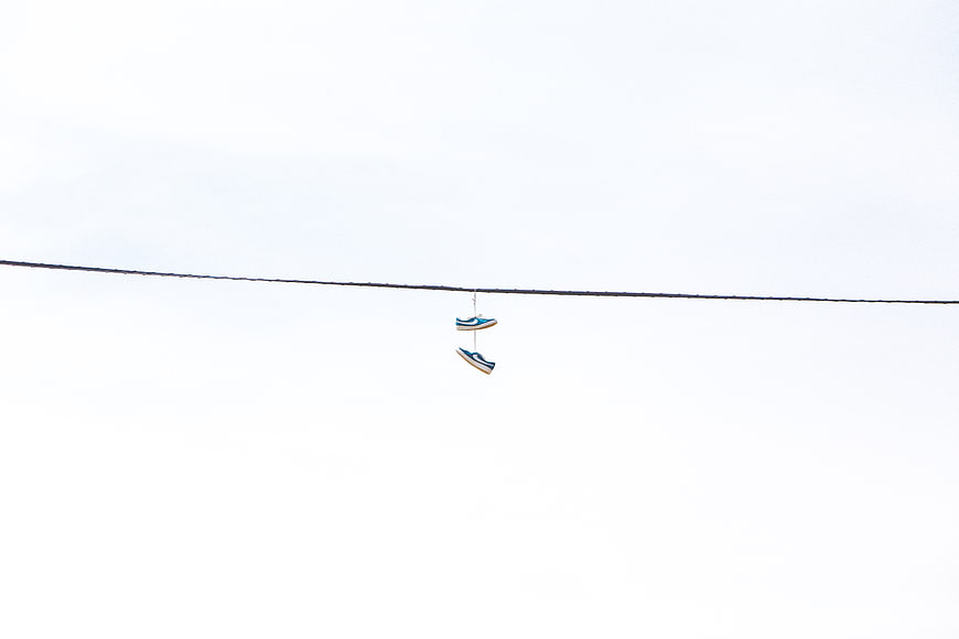 Minimalist sneakers hanging on a wire against white sky