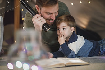 Father and son reading with flashlight in cozy indoor tent