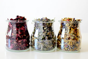 Three glass jars filled with dried rose petals and herbal flower blends