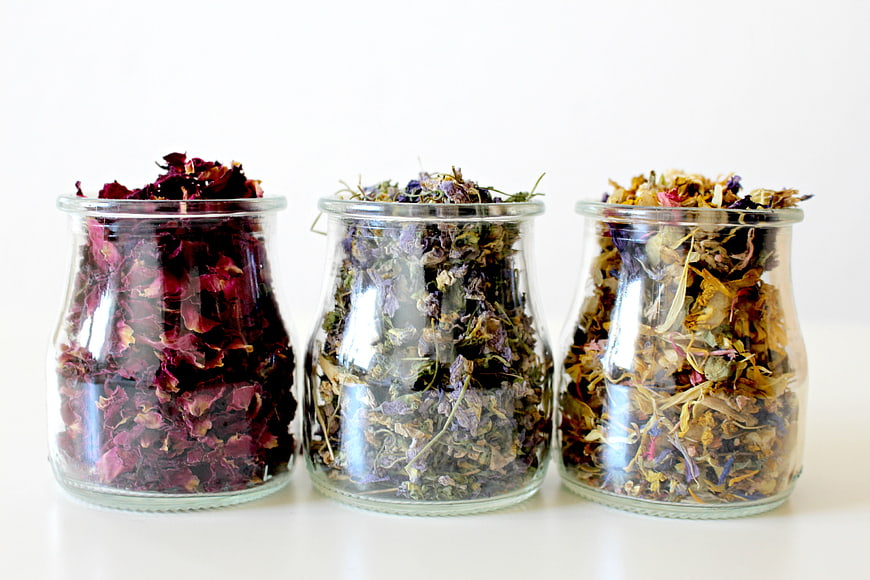 Three glass jars filled with dried rose petals and herbal flower blends