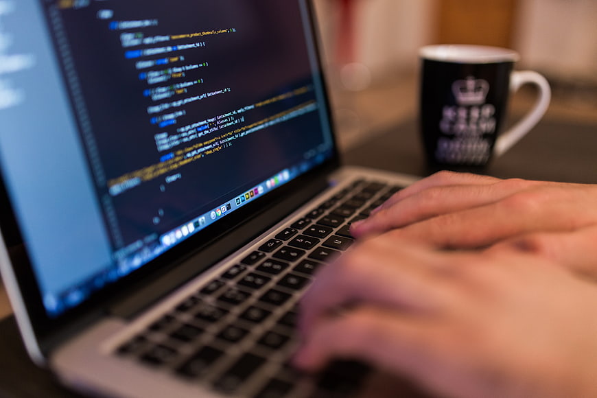 Close-up of hands typing code on laptop with coffee mug