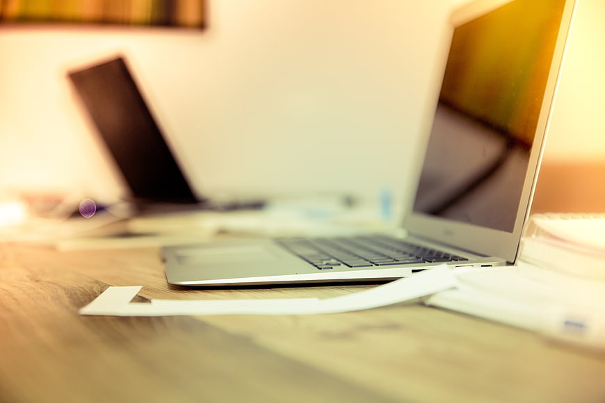 Silver laptop on wooden desk with blurred office background