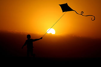 Silhouette of child flying kite at sunset