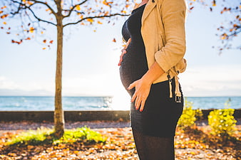 Pregnant woman holding belly outdoors in autumn