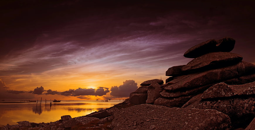 Dramatic Sunset Over Rocky Shoreline with Purple Sky
