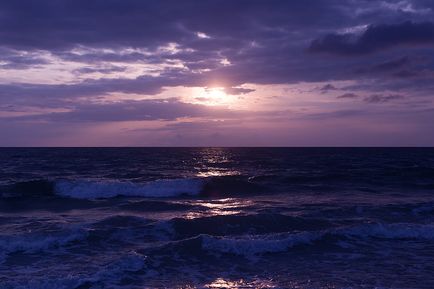 Dramatic purple sunset over ocean waves with cloudy sky