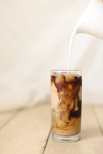 Milk being poured into a glass of iced coffee with ice cubes