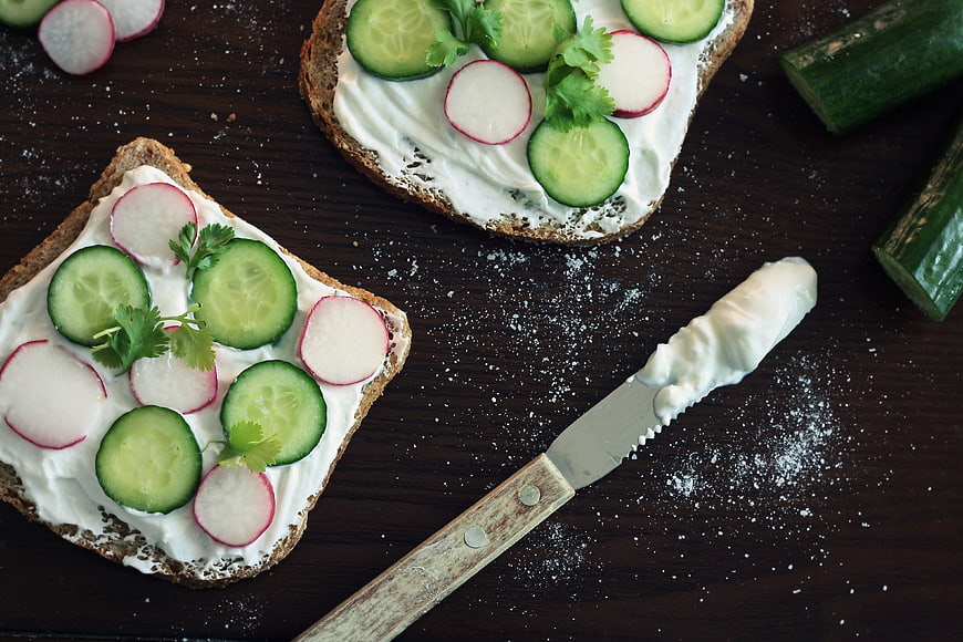 Rustic cucumber and radish toast with yogurt on dark wooden table