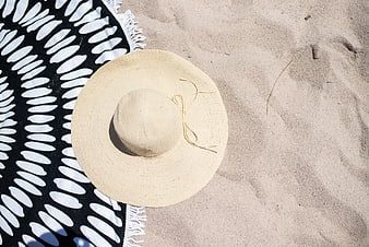 Straw sun hat on black and white beach towel in sand