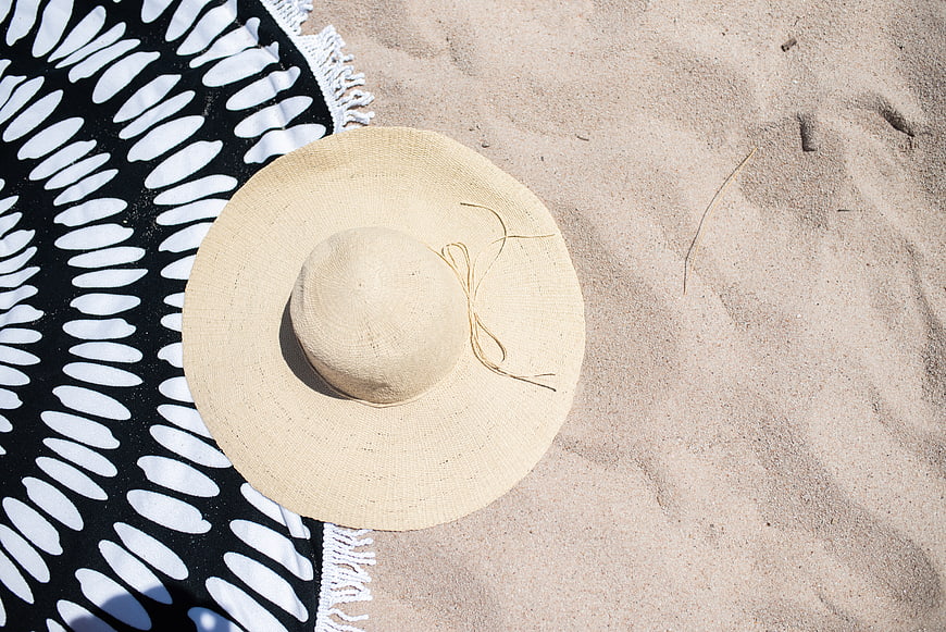 Straw sun hat on black and white beach towel in sand