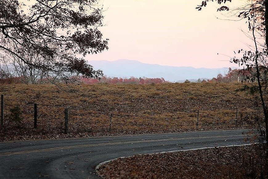 Rural country road winding through autumn landscape with mountains