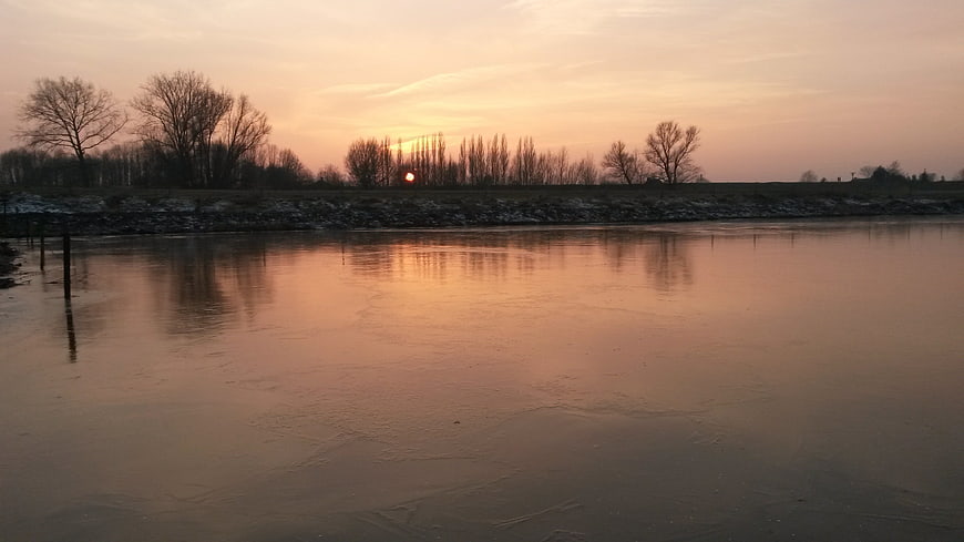Frozen river landscape at sunset with bare trees and ice